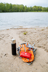 Outdoor adventure essentials for a day out by the lake backpack, thermos, and first aid kit. Stay...