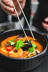 A chef’s hand garnishing a bowl of seafood soup with herbs, capturing the motion and precision in food presentation