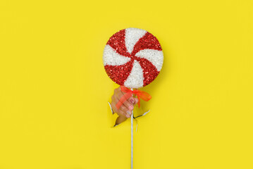 Female hand holding a lollipop emerges from a hole in a torn paper background.