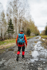 In spring, a backpacker explores a muddy forest trail, surrounded by budding trees and serene...