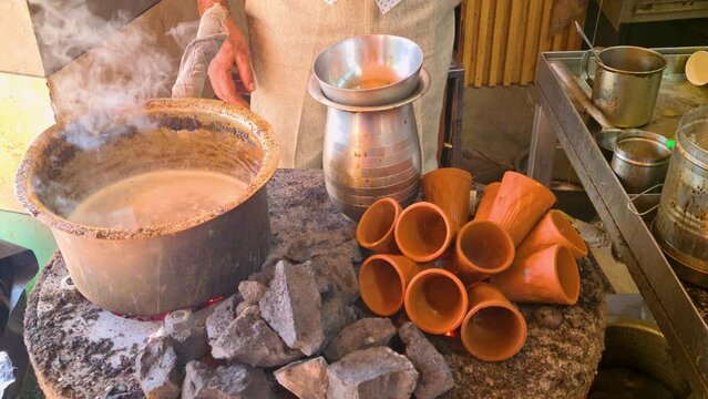 Close up indian man making a pot of tandoori tea over hot coals with clay earthenware cups heating on the side to serve in Jaipur, Delhi, Lucknow