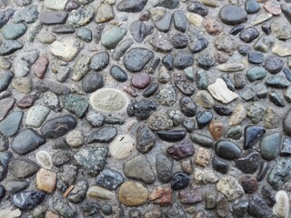 Pebble stone floor tile seamless background. Cement mixed gravel stone floor texture. Wet round pebble stone rock floor with dramatic lighting. Big colorful pebbles on floor after rain near seacoast. 