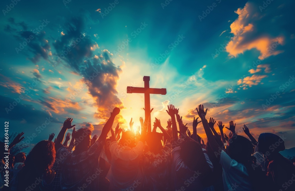 Wall mural A group of people raising their hands in worship, with the silhouette of an cross above them against a sky background. The scene is illuminated by sunlight rays and conveys unity