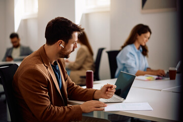 Male entrepreneur taking notes while working on laptop in modern office.