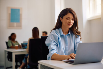 Female entrepreneur using laptop in co-working office.