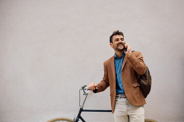 Happy entrepreneur with bicycle talking on the phone against  wall.