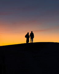 Two people standing on a hill watching the sunset