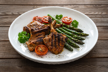 Lamb chops with bone and cooked green asparagus on wooden table
