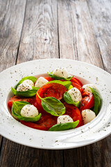 Caprese salad - tomatoes and mozzarella balls served in white bowl on wooden background
