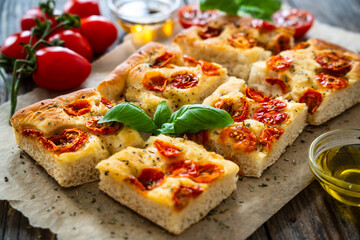 Focaccia - baked sandwich with tomatoes and basil leaves on wooden table