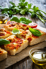 Focaccia - baked sandwich with tomatoes and basil leaves on wooden table