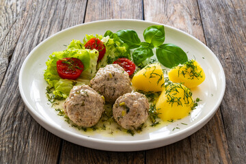 Cooked meatballs in dill sauce with boiled potatoes and fresh vegetables on wooden table
