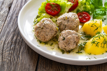 Cooked meatballs in dill sauce with boiled potatoes and fresh vegetables on wooden table
