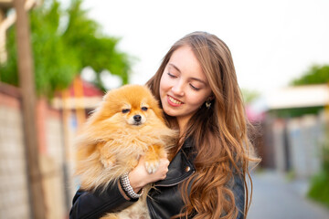 Beautiful young girl with a dog in her arms. Love to the animals. Pet on a walk. Animal protection. Pomeranian Spitz.