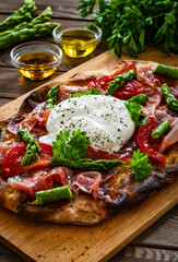 Roman Pinsa with burrata cheese, ripened ham and green asparagus on wooden table
