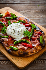 Roman Pinsa with burrata cheese, ripened ham and green asparagus on wooden table

