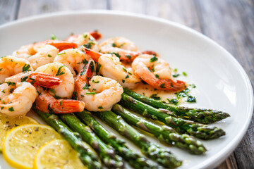 Naklejka premium Fried shrimps with garlic and parsley in olive oil and cooked green asparagus on wooden table 