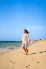 Fototapeta na wymiar Beautiful woman with arms raised and outstretched walking on sunny beach 