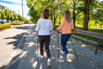 Nordic walking - two mid-adult beautiful women exercising in city park using Nordic walking poles 
