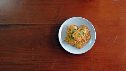 Three golden-brown pieces of tempeh are elegantly presented on a white plate, promising a delicious blend of crunch and flavor. 