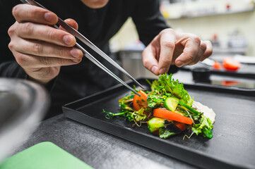 A close-up of hands wearing black gloves carefully plating a gourmet salad with mixed greens,...