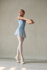 ballerina girl in a blue bodysuit and skirt shows ballet steps