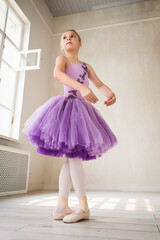 portraits ballerina girl in a lilac dress posing in a room showing ballet poses