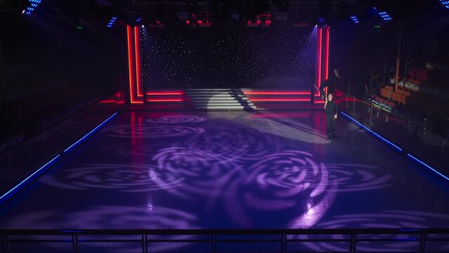 Figure skaters pair perform overhead lift, man holds his partner her with his extended arm slides ice. Her figure upside down, crossed legs and torso are straight. Then he picks up girl in his arms