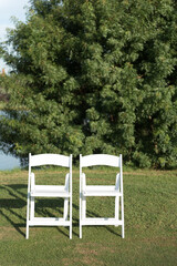 Two chairs placed on a green lawn set up for an outdoor wedding ceremony