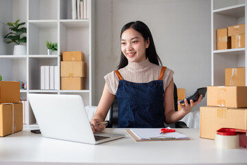 Asian women packing boxes and using a tablet in a home office. Concept of small business and...