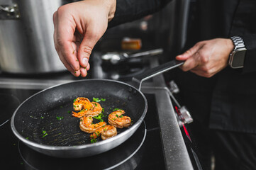 A person cooking shrimp in a pan, seasoning it with herbs