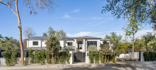 Charming white house sits nestled among lush foliage of trees and bushes on a peaceful street