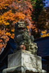 Green traditional asian stone statue on building near autumn foliage