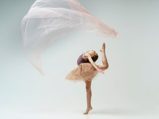 young teenage ballerina girl shows elements of dance with fabric in a photo studio