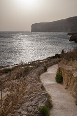 a walkway leading to the beach at sunset by a rocky path: Xlendi Bay in Gozo island in Malta