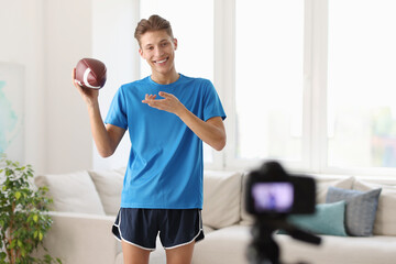 Smiling sports blogger holding american football ball while recording fitness lesson with camera at home