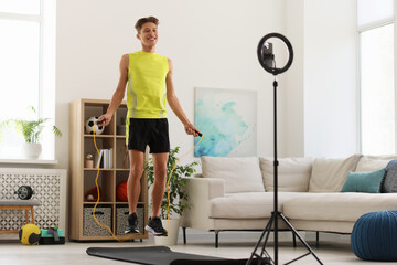 Smiling sports blogger jumping with rope while streaming online fitness lesson with smartphone at...