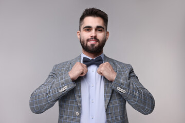 Portrait of smiling man adjusting bow tie on grey background