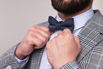 Man adjusting bow tie on grey background, closeup