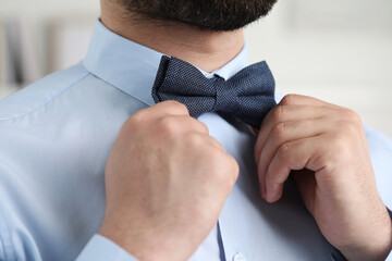 Man in shirt adjusting bow tie indoors, closeup