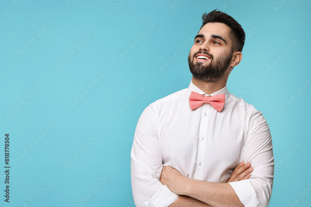 Wall mural Portrait of smiling man in shirt and bow tie on light blue background. Space for text