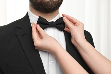 Woman adjusting bow tie to man indoors, closeup