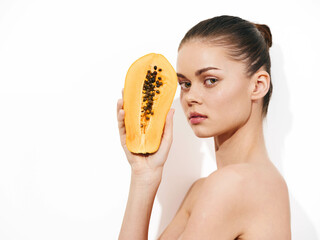 Woman holding papaya in front of face, gazing at camera with curiosity and wonder, tropical fruit...
