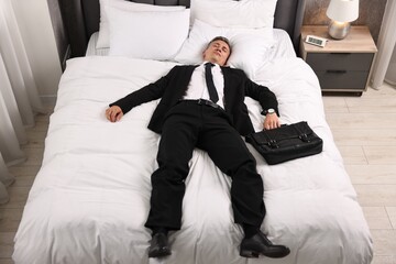 Businessman with briefcase sleeping on bed indoors