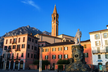Town square with statue, colorful buildings, and clock tower against mountain backdrop