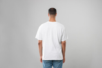 Man wearing white t-shirt on gray background, back view - Powered by Adobe