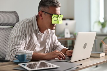 Man with fake eyes painted on sticky notes using laptop in office