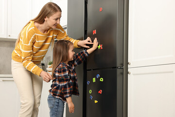 Mom and daughter putting magnetic letters on fridge at home. Learning alphabet