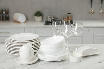 Clean plates, bowls, cups and glasses on white marble table in kitchen