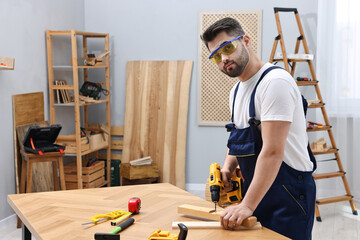 Young worker using electric drill at table in workshop